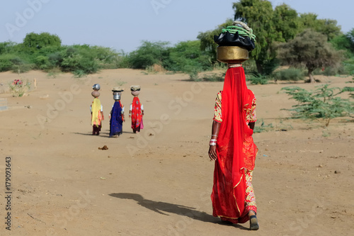 Indian ethnic women carries jar on her head and going for the water in well on the desert. Rajasthan, India. Thar desert near Jaisamler