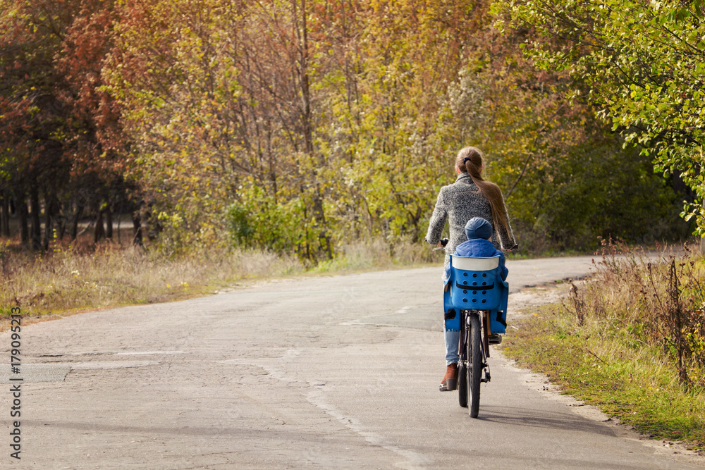 Mom and son are riding a bicycle on the autumn road. Back view.