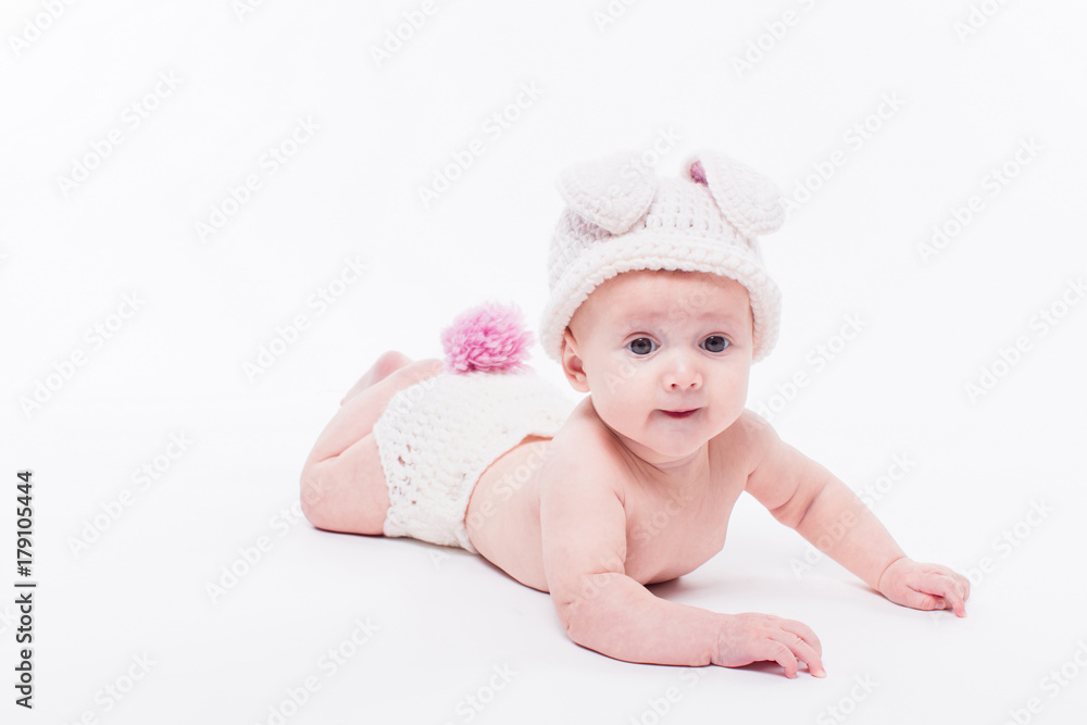 Cute baby girl lying naked on a white background wearing a hat in the form of a Christmas bunny with pink ears and tail Cute baby girl lying naked on a white background wearing a hat in the form of a Christmas bunny with pink ears and tail