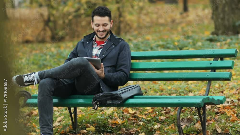 Portrait happy smiling casual caucasian man making video call holding tablet computer waving palm autumn beautiful park background sitting bench calling online 3g browser connect bearded guy greeting Portrait happy smiling casual caucasian man making video call holding tablet computer waving palm autumn beautiful park background sitting bench calling online 3g browser connect bearded guy greeting