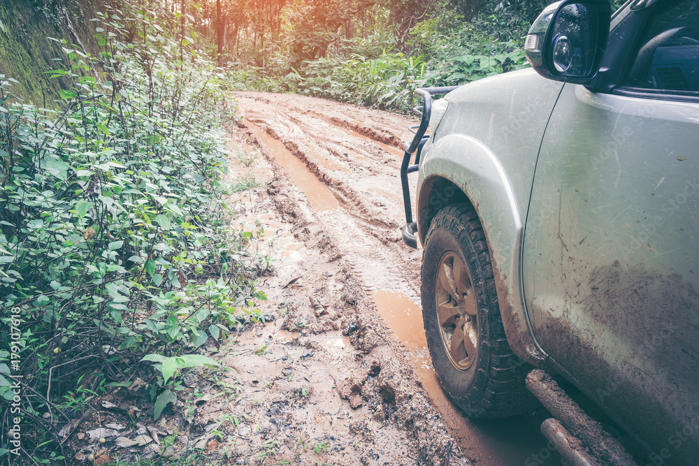 Car wheel on a dirt road. Off-road tire covered with mud, dirt terrain. Outdoor, adventures and travel suv. Car tire close-up in a countryside landscape with a muddy road. Four wheel truck in mud.
