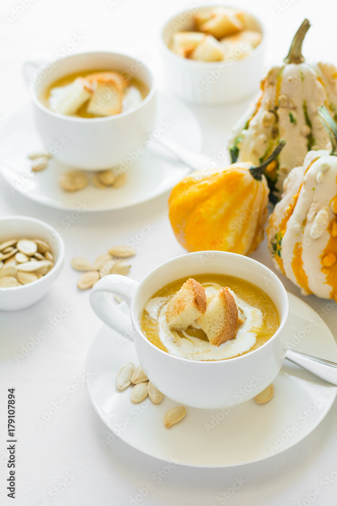 Two cups with fresh pumpkin cream soup decorated cream, seeds and crackers on white table cloth Two cups with fresh pumpkin cream soup decorated cream, seeds and crackers on white table cloth