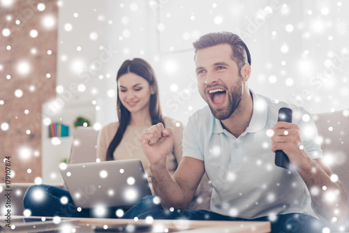 Married young people are spending their weekend at home together. He is watching game and she is searching for information in her laptop, snowflakes background