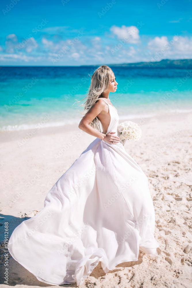 Beautiful bride in long white dress on the beach with white bouquet Beautiful bride in long white dress on the beach with white bouquet