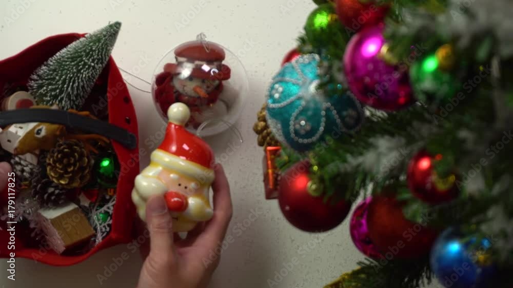 Greeting Season concept. Hand setting of Christmas tree and decorations with presents and ornaments on white wood table from above with falling snow in 4k (UHD) Greeting Season concept. Hand setting of Christmas tree and decorations with presents and ornaments on white wood table from above with falling snow in 4k (UHD)