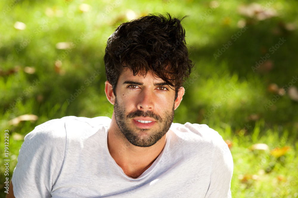 Fototapeta premium Close up serious handsome man with beard sitting in grass