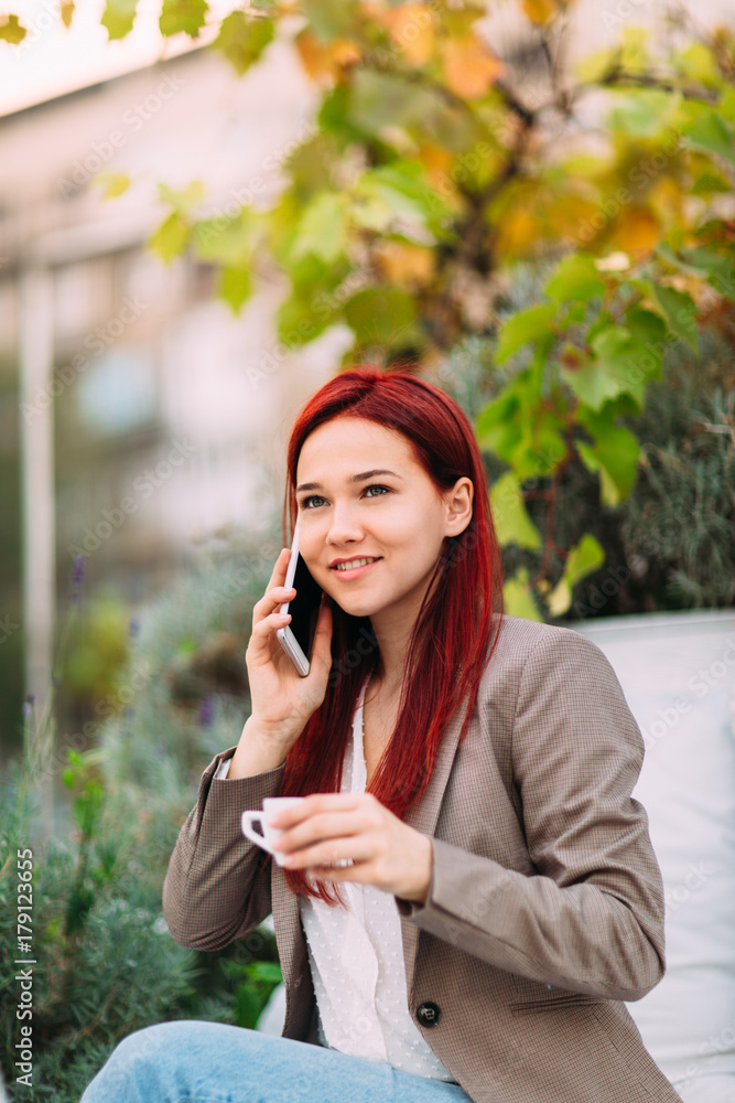 Young redhead woman talking on mobile phone and drinking coffee Young redhead woman talking on mobile phone and drinking coffee