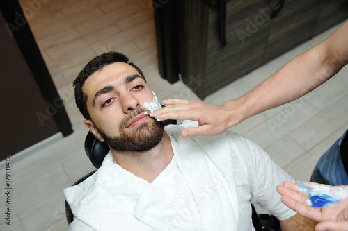 The hairdresser prepares the face for shaving and smears the face with foam