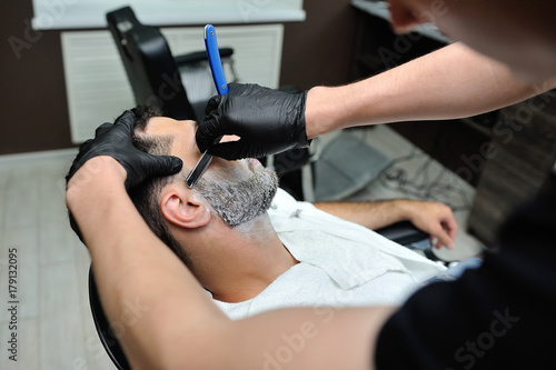 Hairdresser shaves man's beard with a blade in a male barber shop