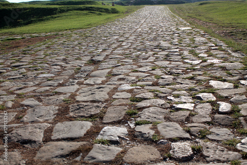 Ancient road paved with cobblestone and going up through hills.
