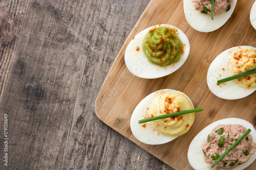 Variety of stuffed eggs with avocado and tuna on wooden table.Top view