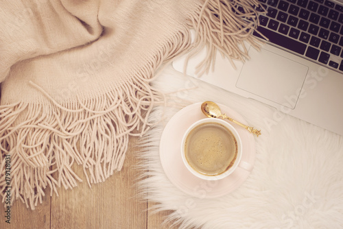 Cozy Winter Mornings. Coffee, laptop and a warm scarf on a white fur carpet on the floor