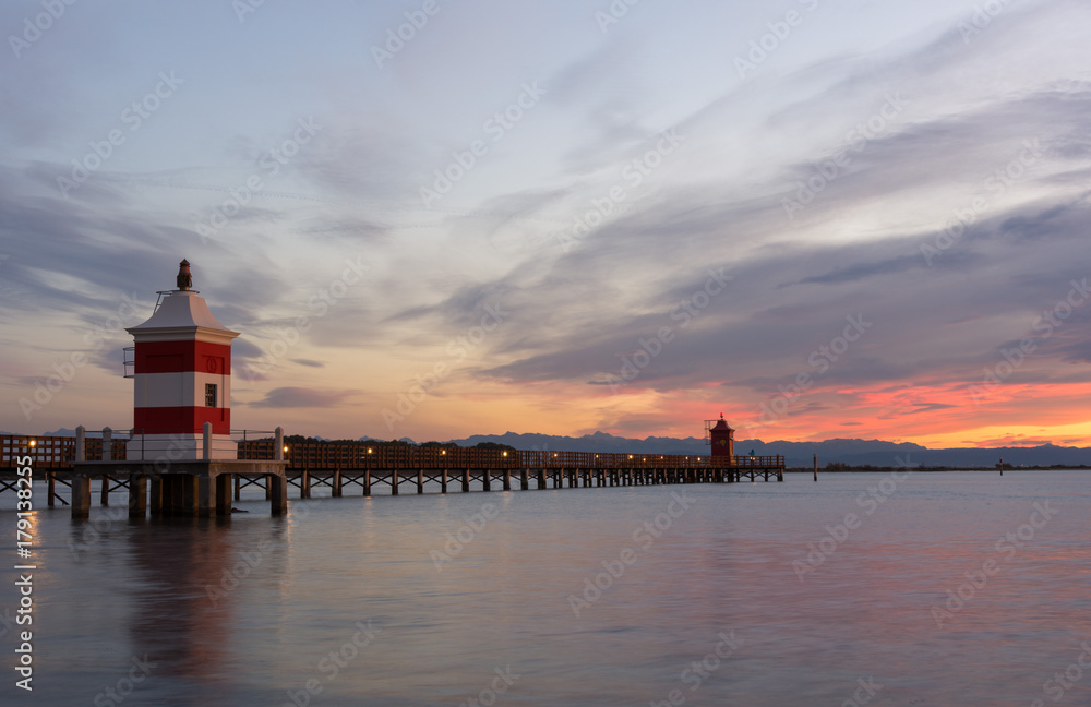 Beautiful sunrise at the seaside in Italy, at Lignano Sabbiadoro, with pier and lighthouse in the foreground.