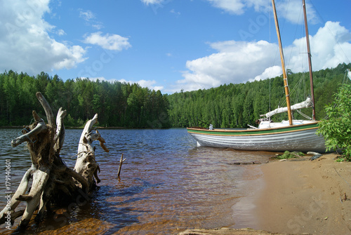 Fényképezés a view of the lake bay with a bizarre snag in the water in the foreground and two half-dragged ashore sailing boats