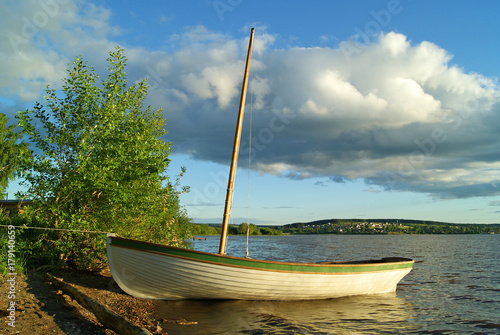 Vászonkép Wooden skiff with a deflated sail, moored on the unequipped shore of the lake