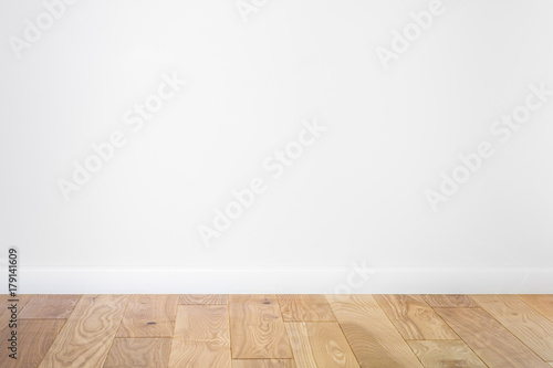White painted stucco wall and natural wooden ash-tree 3-band parquet board hardwood floor. Flooring in scandinavian style of empty interior with wide white baseboards. Light brown, biscuit color.