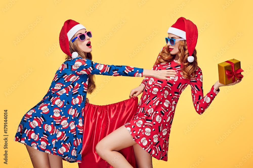 New Year. Young Woman and Santa Bag with Presents Having Fun Happy Smiling. New Year Fashion. Playful Sisters Best Friends in Stylish fashion Red Xmas Holiday Dress on Yellow. Christmas Colorful
