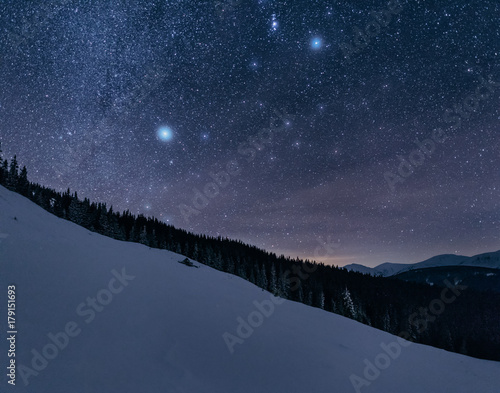 Winter landscape of a mountain range at night. Stars over the mountain range. Snow covers slopes of a mountains. © ianachyrva