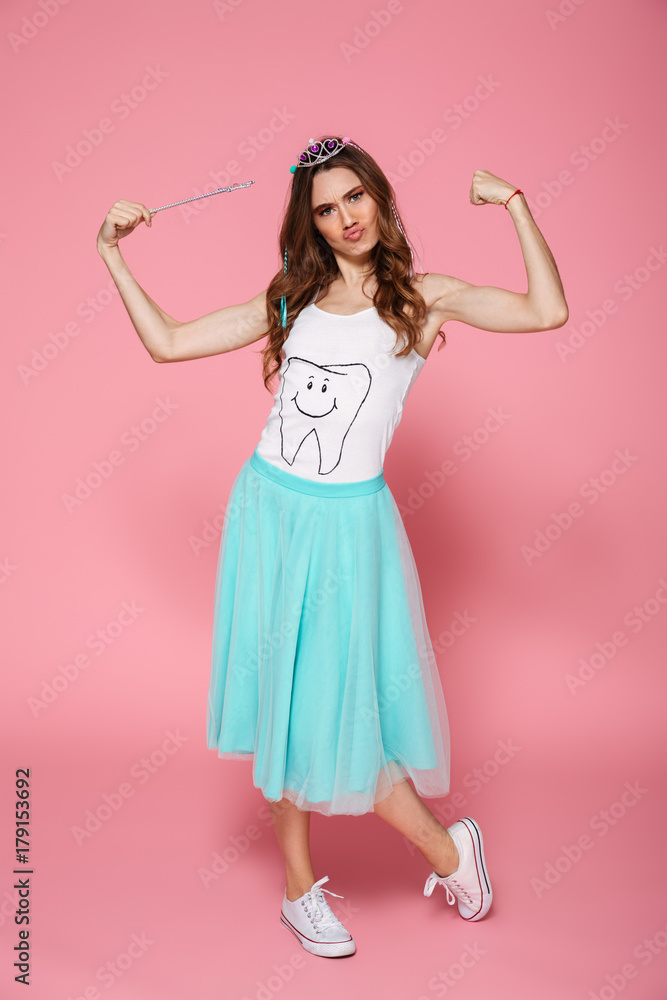 Full length portrait of funny young woman dressed like princess holding magic wand, showing her small muscles Full length portrait of funny young woman dressed like princess holding magic wand, showing her small muscles
