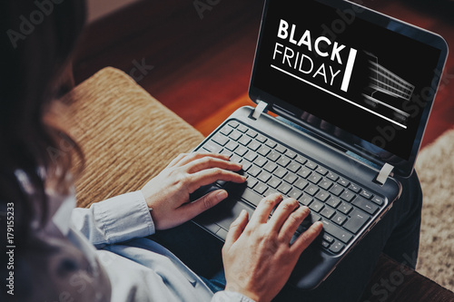 Black Friday advertisement in a laptop screen while woman uses it to buy by internet at home.