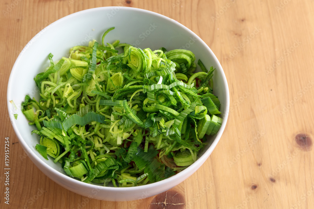 sliced fresh leek in a white bowl on a wooden table, ingredient to cook with healthy vegetables