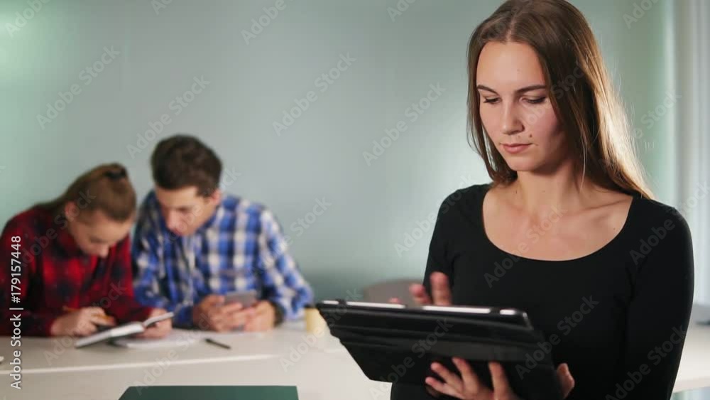 An attractive young woman standing in the office and using her tablet while her colleagues are working on the blurred background. Slowmotion shot An attractive young woman standing in the office and using her tablet while her colleagues are working on the blurred background. Slowmotion shot