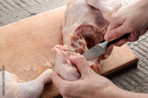 girl knives a raw chicken into pieces on a cutting board.