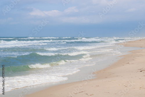 Sea coast waves rolling on sandy beach  stormy cloudy sunrise