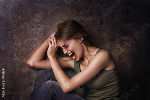 Battered young woman sitting near wall photo