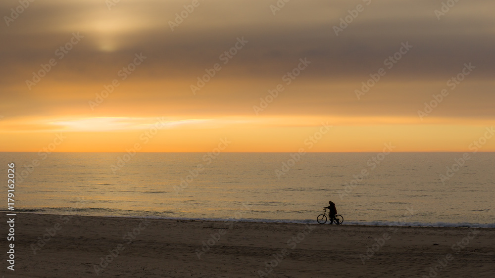 Nastrojowe zdjęcie rowerzysty na tle zachodu słońca na plaży nad morzem.