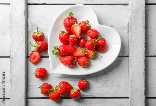 Heart shaped plate with strawberries on wooden background