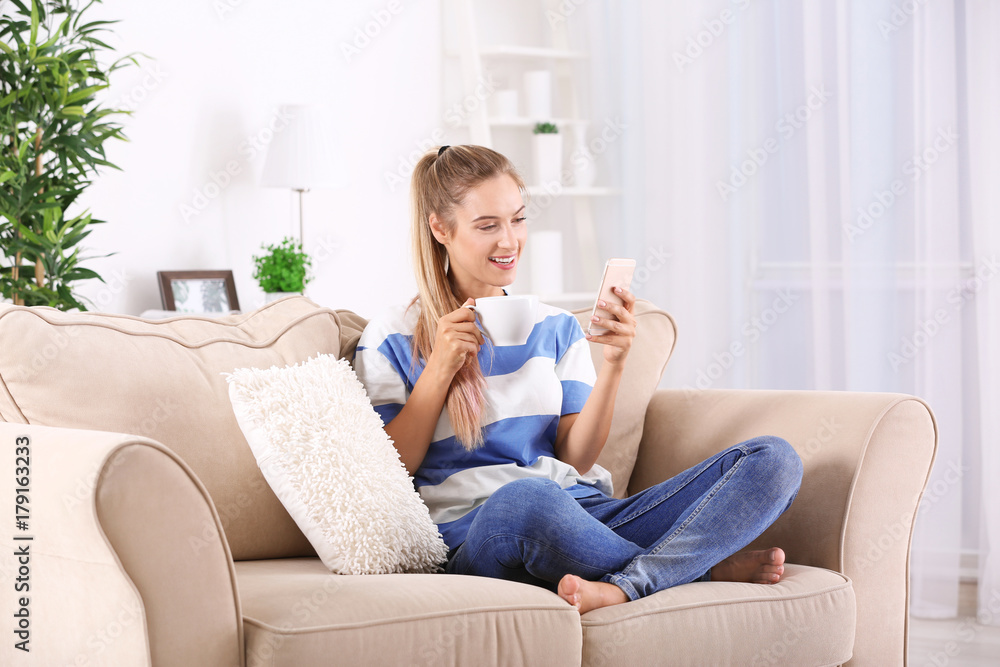 Young woman using smartphone while drinking tea at home Young woman using smartphone while drinking tea at home