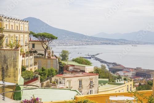 Panorama del golfo di Napoli dal quartiere collinare Vomero. Sullo sfondo si vede il vulcano Vesuvio che domina sulla città e il porto che si affaccia sul golfo di Napoli. Un palazzo copre la vista.