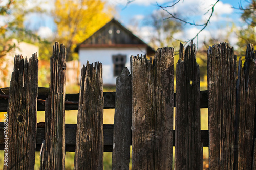 An old-time small white house fenced with an old wooden fence in the style of ancient Ukrainian traditions