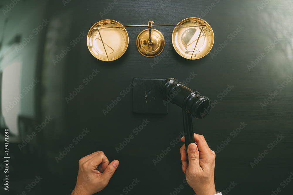 justice and law concept.Top view of Male judge hand in a courtroom with the gavel and brass scalr on dark wood table