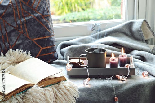 Cozy home with cup of tea with steam, blanket, book and candles. Hygge home interior photo