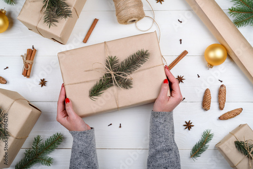 Christmas gift wrapping background. Female hands packaging christmas present wrapped in kraft paper, top view. Winter holidays concept, flat lay. Woman holding Christmas gift box