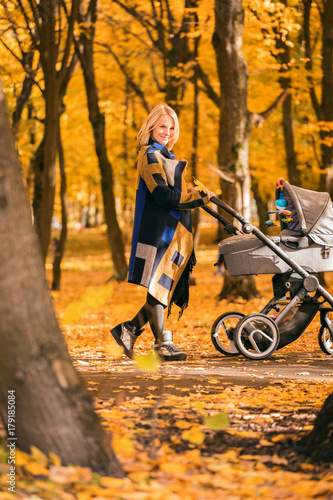 A young mother with a stroller walks through the autumn park. Walking with an infant in the open air in a pine forest. Newborn, family, child, parenthood. © LALSSTOCK