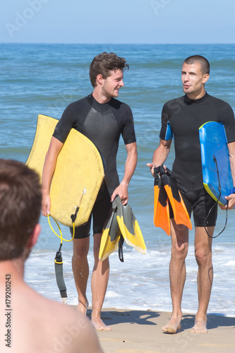 boys carry bodyboards on the shore of beache photo