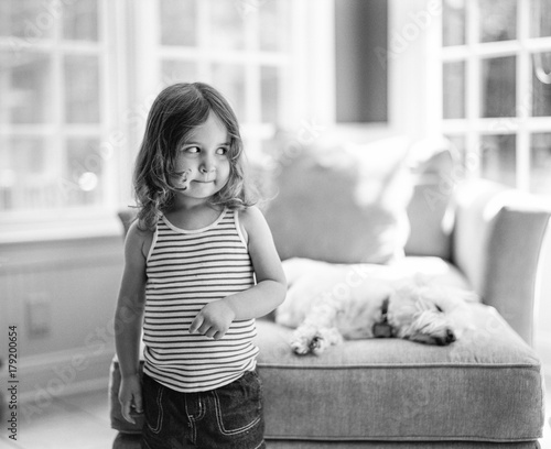 A toddler looking mischievous with a dog sleeping behind her