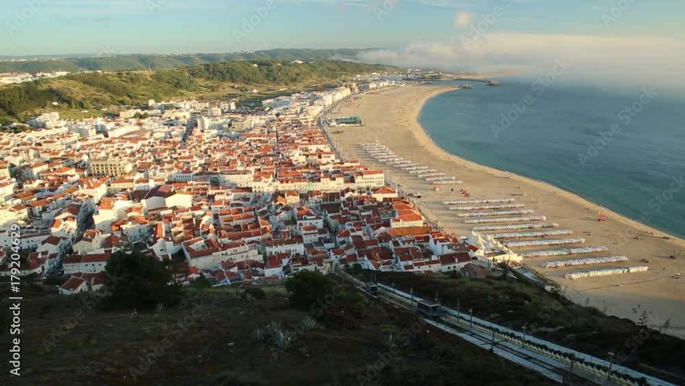 Moving trains of Railway Funicular in sunset skyline and beach waterfront from Miradouro do Suberco in Nazare Sitio, upper town above the giant cliffs in Central Portugal, Europe. Moving trains of Railway Funicular in sunset skyline and beach waterfront from Miradouro do Suberco in Nazare Sitio, upper town above the giant cliffs in Central Portugal, Europe.