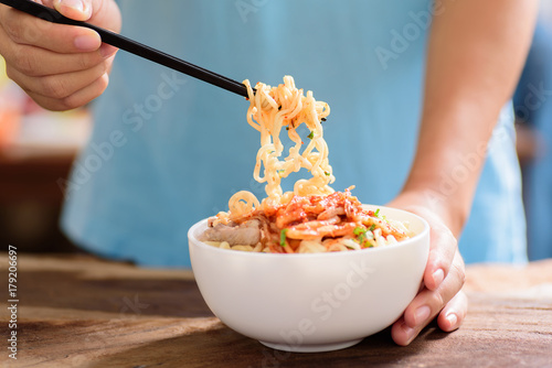 Korean food,hand holding chopsticks for eating instant noodle with kimchi cabbage in a bowl on wooden background