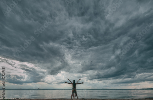 Young man and woman standing in a pose of Leonardo da Vinci Vitruvian Man against dramatic sky.