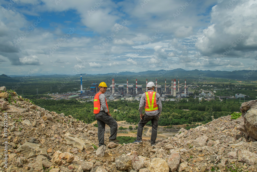 Engineer and construction site manager dealing with a coal power plant in the background.