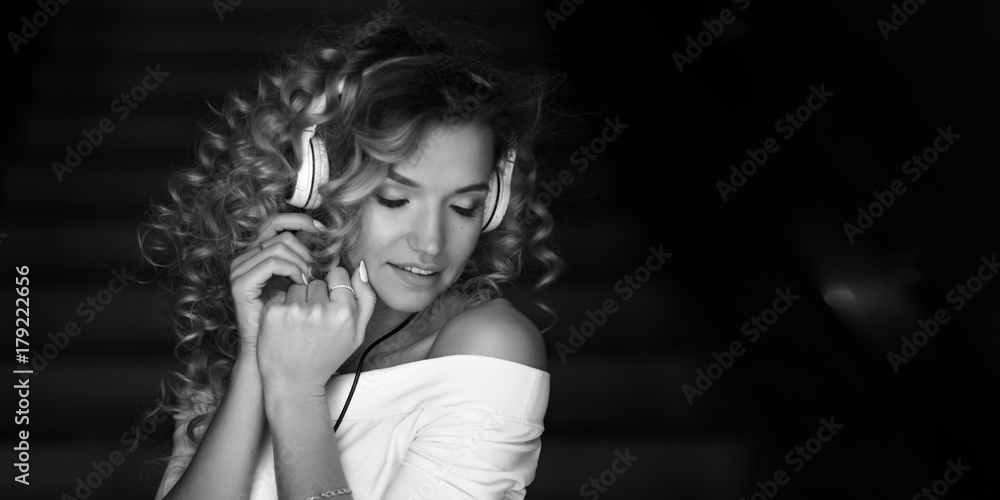 Portrait of a curly girl in headphones. She listens to music and dances. Black and white photo. Portrait of a curly girl in headphones. She listens to music and dances. Black and white photo.