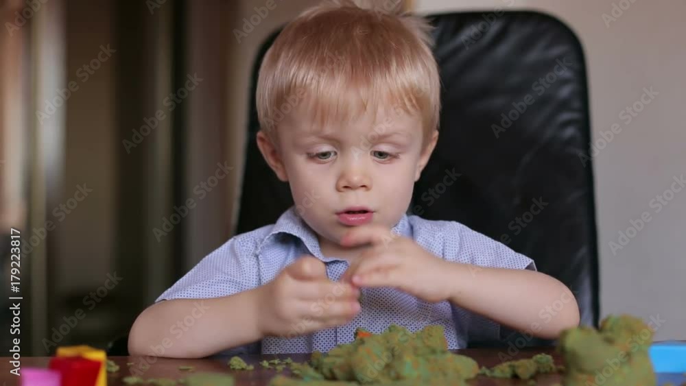 Happy smiling child plays kinetic sand at home. Little boy three years playing with kinetic sand at home, close-up. Happy smiling child plays kinetic sand at home. Little boy three years playing with kinetic sand at home, close-up.