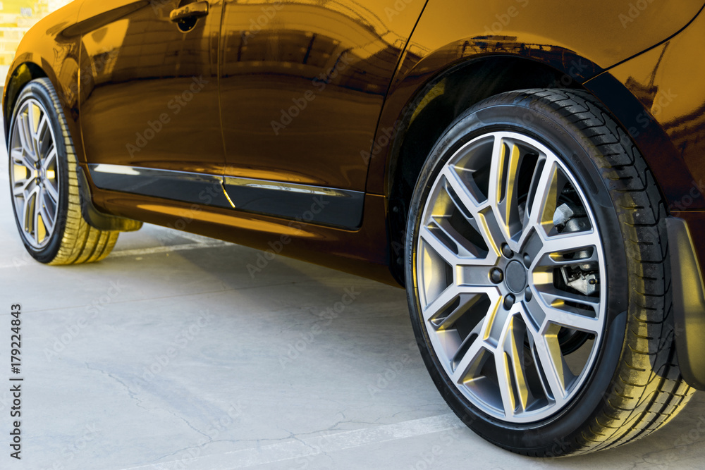 Side view of a car. Tire and alloy wheel of a modern gold car on the ground at the sunset. Car exterior details