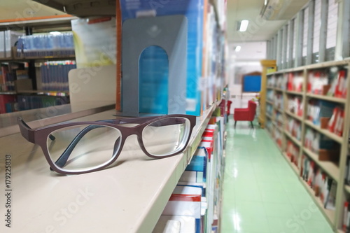 A glasses on the bookshelf in the library. Selective focus with blurred bookshelves background and vintage style picture. Education concept.