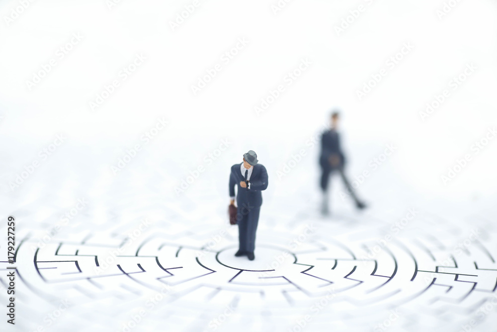 Miniature people: Businessman standing on center of maze Miniature people: Businessman standing on center of maze