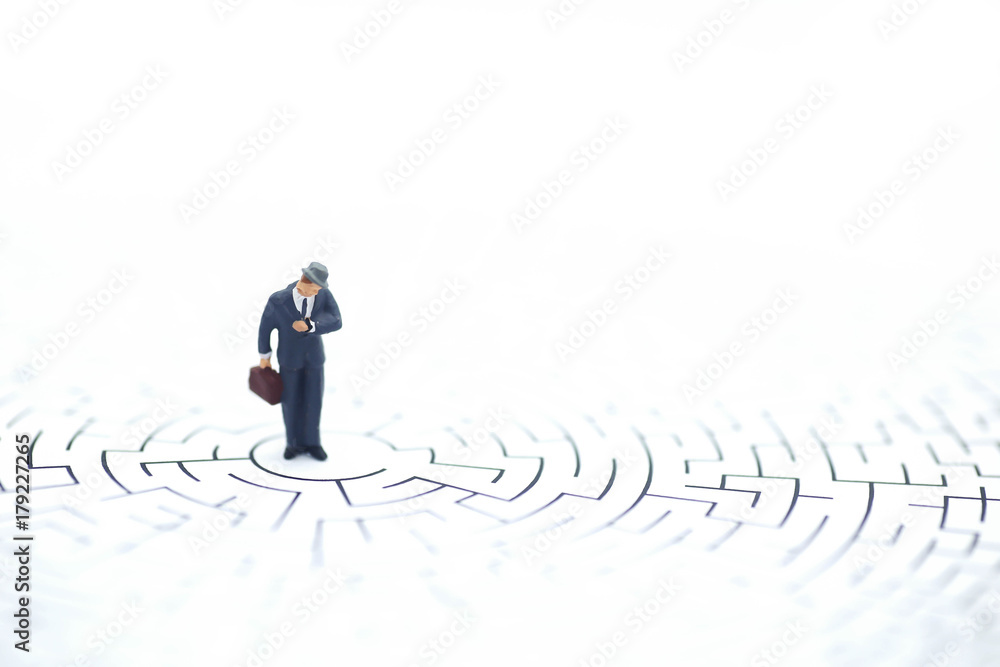 Miniature people: Businessman standing on center of maze Miniature people: Businessman standing on center of maze